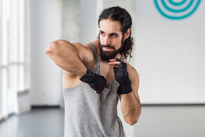 Portrait of angry muscular young adult man with curly hair standing and preparing to fight with elbow in black gloves, showing stock photography Portrait of angry muscular young adult man with curly hair standing and preparing to fight with elbow in black gloves, showing stock photography