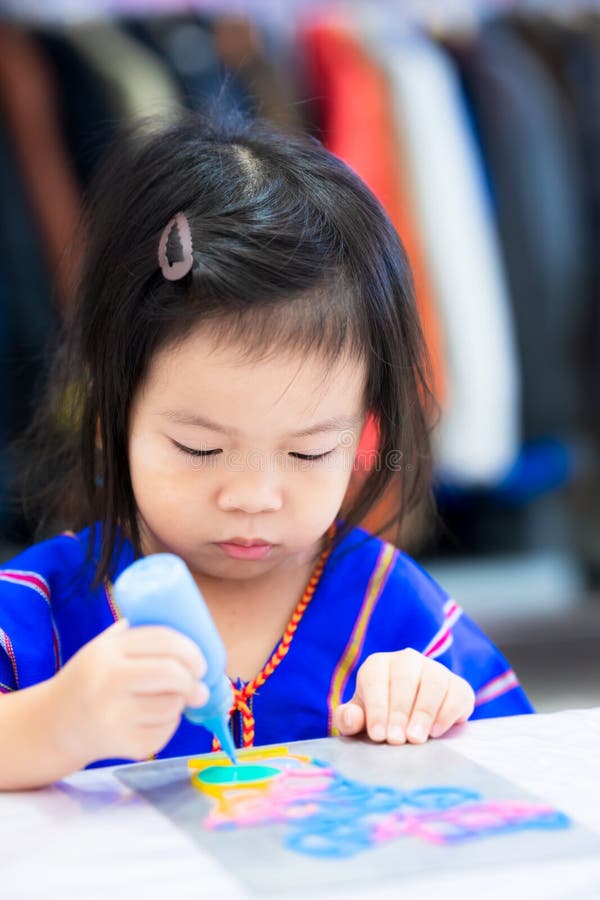 Portrait Asian child girl doing art. Kid holding blue color bottle in her hand. Children aged 3 years old making craft