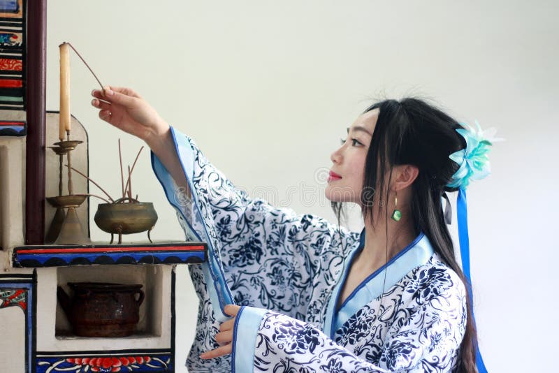 Portrait of Asian Chinese girl in traditional dress, wear blue and white porcelain style Hanfu, Light the candles on the stove