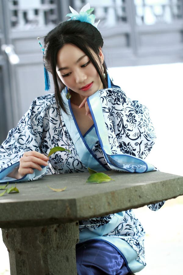 Portrait of Asian Chinese girl in traditional dress, wear blue and white porcelain style Hanfu, sit on a stone chair