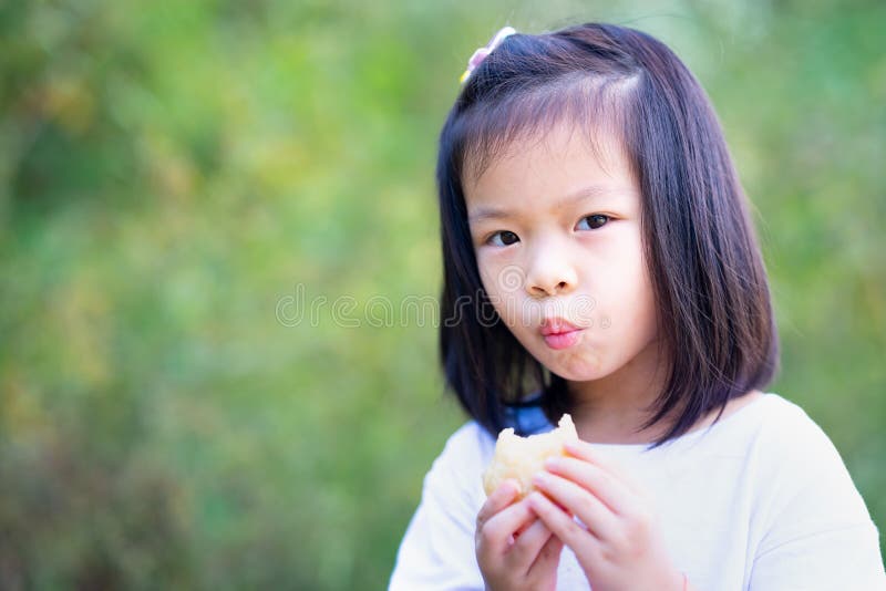 Portrait Asian kid girl bite fried bread. Child is hungry snack. Brunch time.