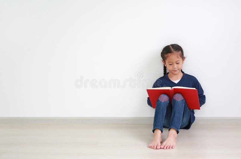 Portrait asian little kid girl in school uniform reading a book and sitting against white wall in the room with copy space
