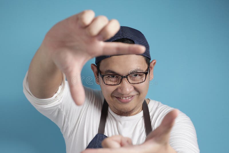 Portrait of Asian male chef or waiter looking at camera and smiling while framing his face with hands