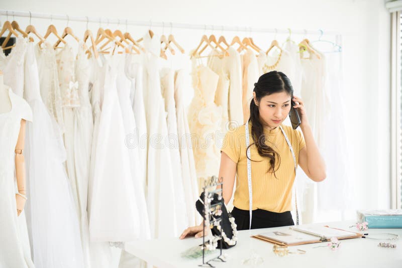 Portrait of asian woman working and using mobilephone in wedding dress store,Beautiful dressmaker in shop and small business owner