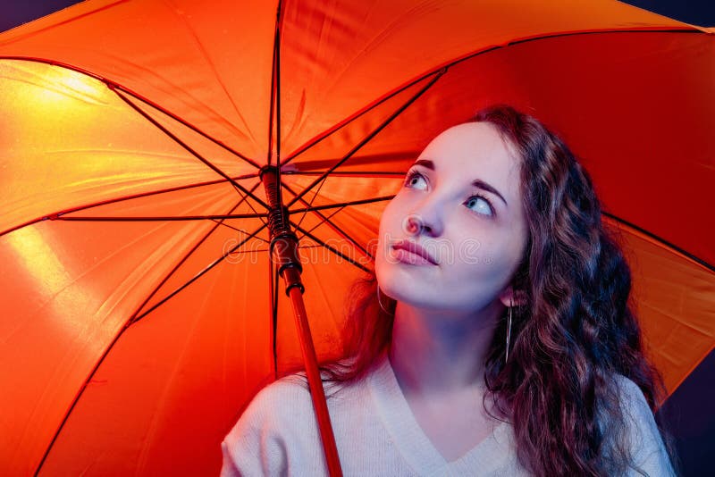 Portrait of attractive girl with colored highlights on her face from street lamps and lightning under a yellow umbrella