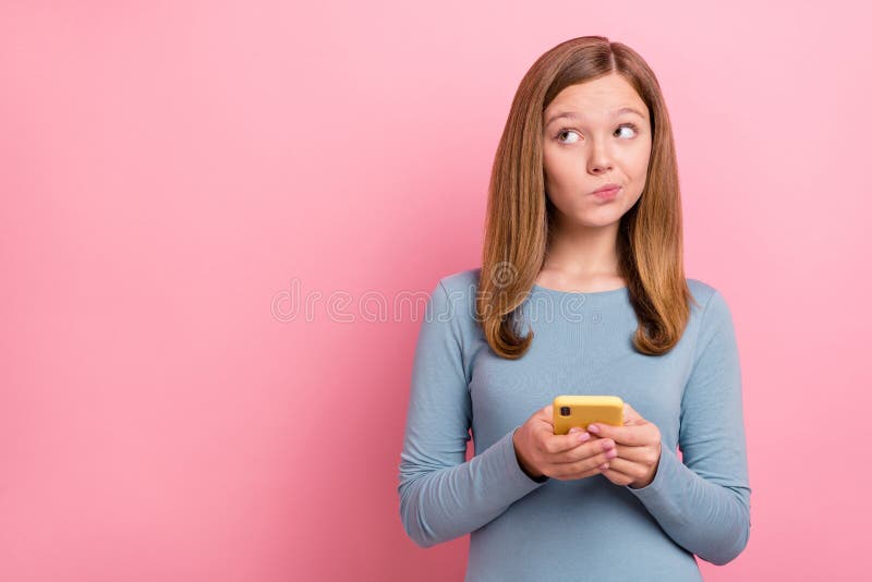 Portrait of attractive minded unsure girl using gadget deciding copy blank space isolated over pink pastel color