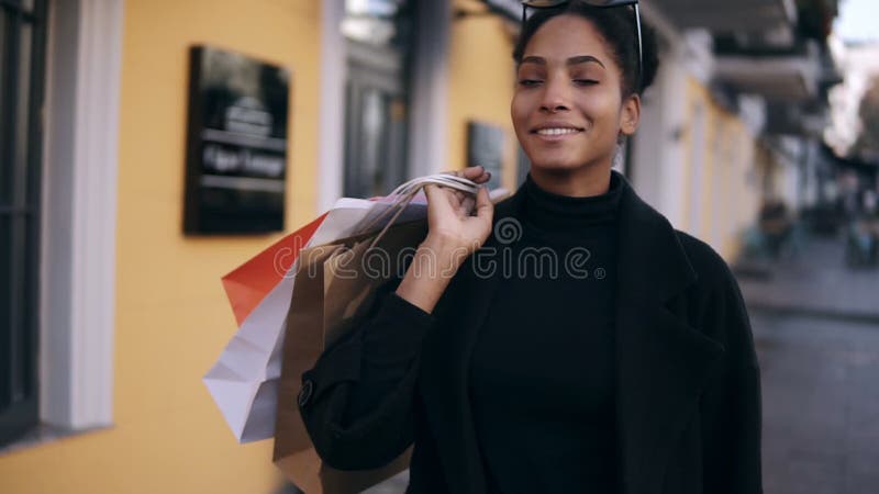 Portrait of an attractive mixed race girl smiling while walking down the street with colorful shopping bags. Happy young