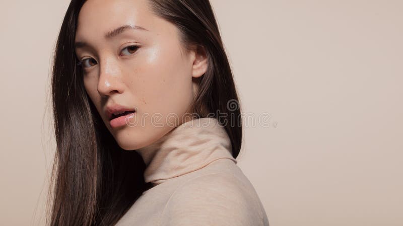 Portrait of attractive young asian woman with brown hair against beige background. Korean female model looking at camera. Portrait of attractive young asian woman with brown hair against beige background. Korean female model looking at camera