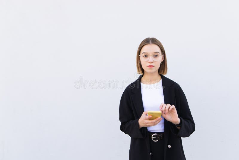 Portrait attractive young business woman standing with a smartphone in her hands against the background of a white wall royalty free stock image Portrait attractive young business woman standing with a smartphone in her hands against the background of a white wall royalty free stock image