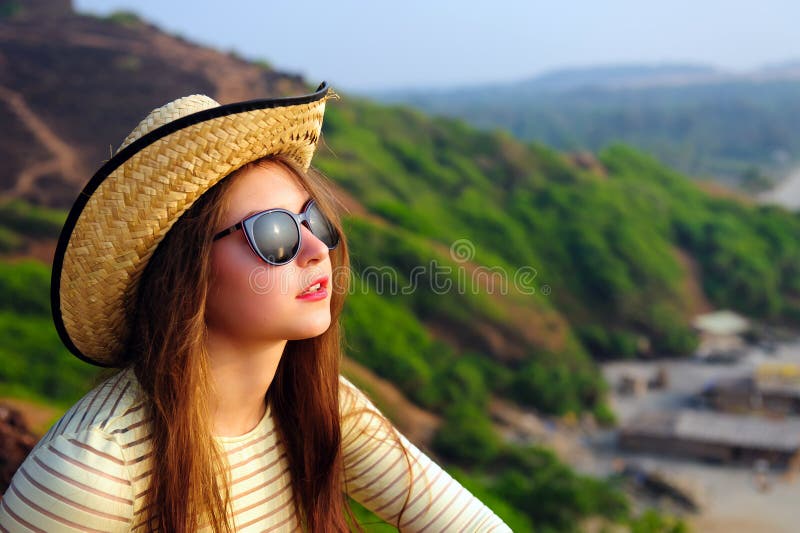 Portrait of an attractive young girl with long hair in straw hat and sunglasses on background of green hills. Selective focus royalty free stock photo Portrait of an attractive young girl with long hair in straw hat and sunglasses on background of green hills. Selective focus royalty free stock photo