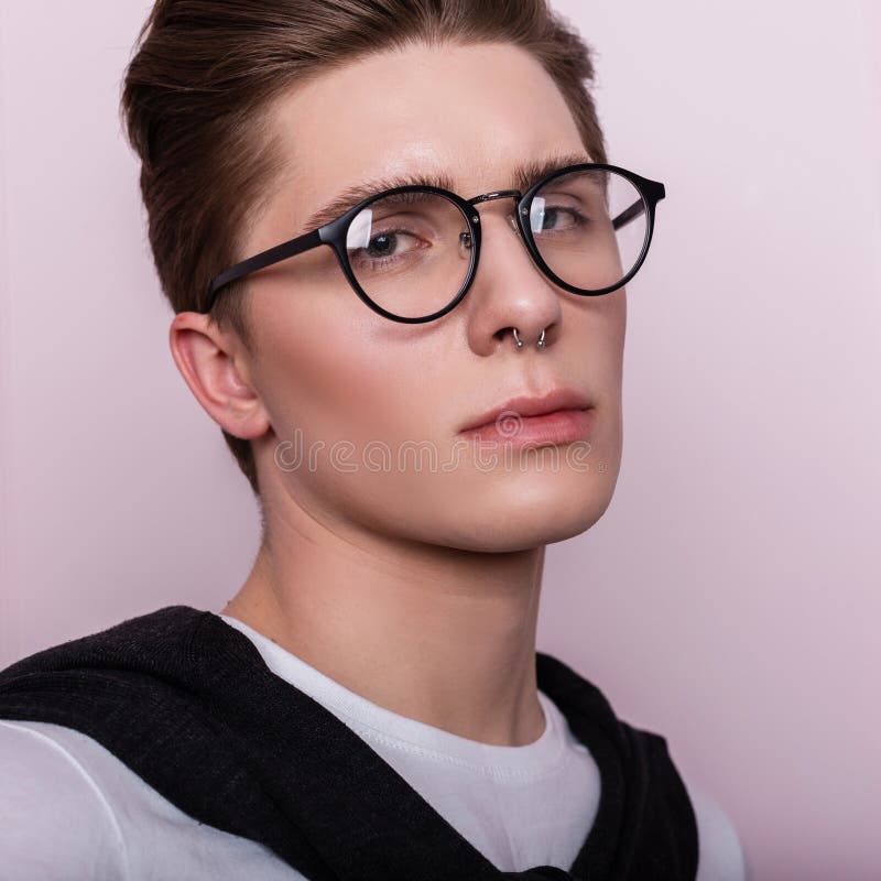 Portrait of an attractive young hipster man in a glasses in a white fashionable t-shirt with a hairstyle near a vintage wall.