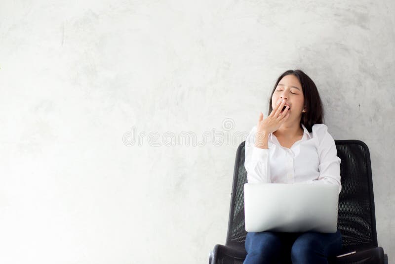 Portrait of beautiful asian young woman yawn at her work place with laptop computer on cement background stock photo Portrait of beautiful asian young woman yawn at her work place with laptop computer on cement background stock photo