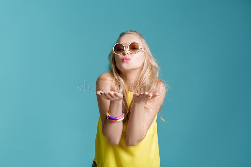 Portrait of beautiful blond woman in sunglasses and yellow shirt on blue background. girl sending air kiss royalty free stock photos Portrait of beautiful blond woman in sunglasses and yellow shirt on blue background. girl sending air kiss royalty free stock photos