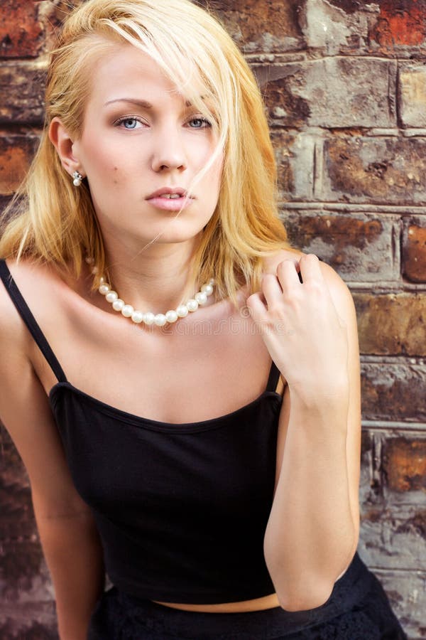 Portrait of a beautiful blonde girl with blue eyes against the wall on the streets of the city on a summer day royalty free stock photo