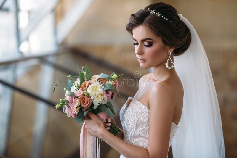 Portrait of beautiful bride with bouquet flowers in white luxury dress. Gorgeous model with bridal makeup and hairstyle