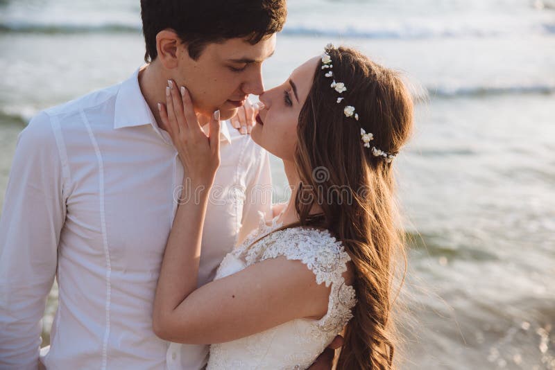 Portrait of beautiful bride and groom on ocean beach. Young couple of newlyweds looking at each other in love