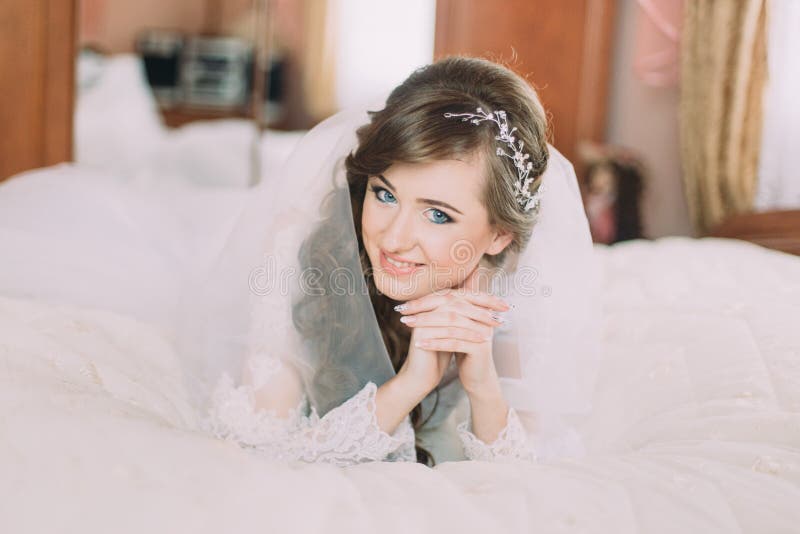 Portrait of beautiful bride in veil with curly hairstyle lying on bed royalty free stock image Portrait of beautiful bride in veil with curly hairstyle lying on bed royalty free stock image