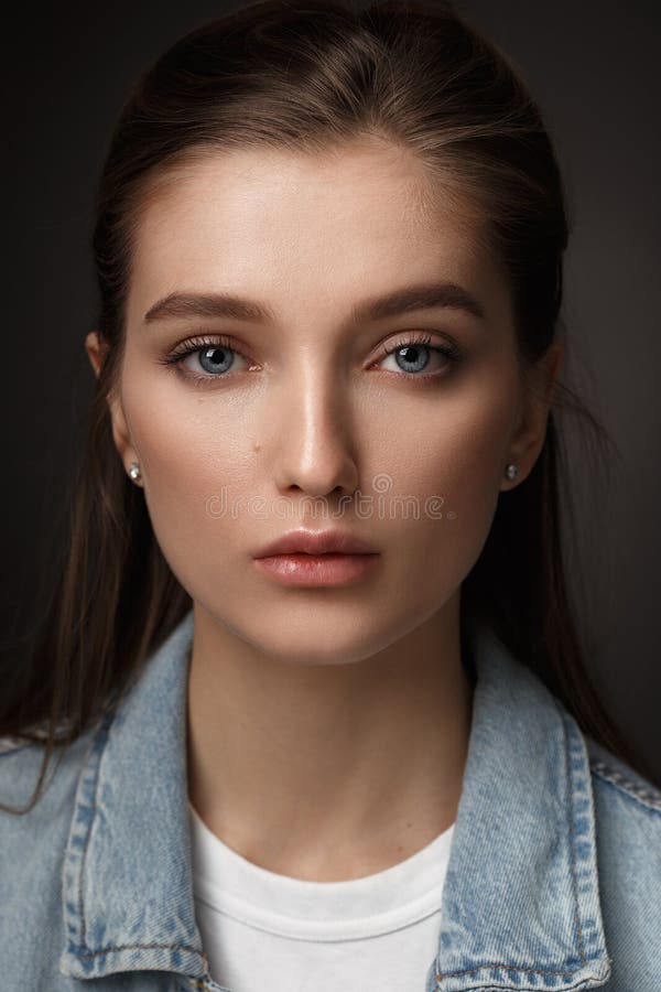 Portrait of beautiful brunette girl with hair tied back dressed in jeans jacket on the dark background in the studio stock photos Portrait of beautiful brunette girl with hair tied back dressed in jeans jacket on the dark background in the studio stock photos