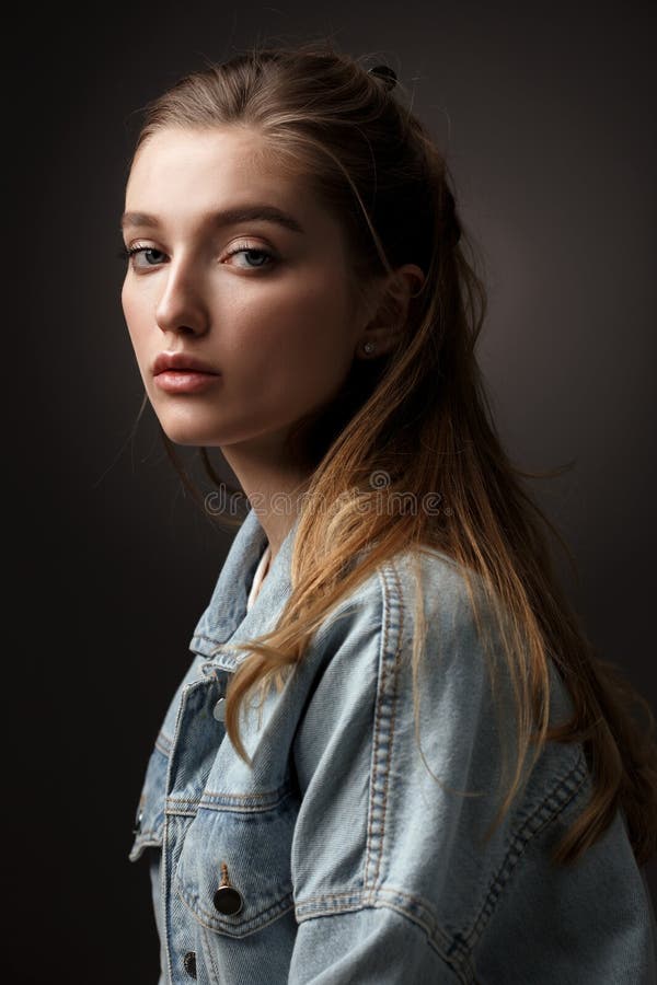 Portrait of beautiful brunette girl with hair tied back dressed in jeans jacket on the dark background in the studio royalty free stock photos Portrait of beautiful brunette girl with hair tied back dressed in jeans jacket on the dark background in the studio royalty free stock photos