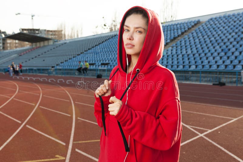 Portrait of a beautiful Caucasian girl athlete on a summer morning jog. A woman is wearing a red fashionable hoodie hoodie. Summer Sport Fitness Healthy Lifestyle