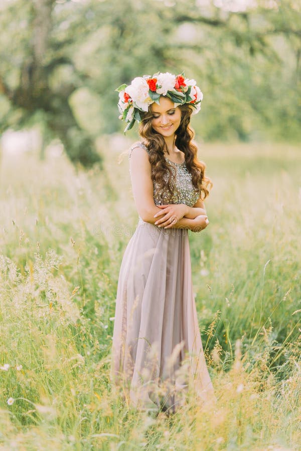 Portrait of beautiful charming young lady in flower wreath and white violet dress looking down