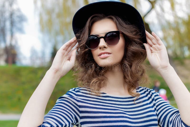 Portrait of a beautiful cute young smiling girl in a black hat and sunglasses in an urban style