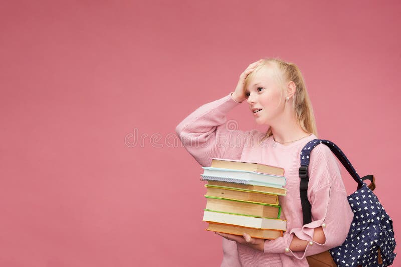 Portrait of a beautiful girl student with a backpack and a stack of books in his hands is smiling at the pink background royalty free stock photo Portrait of a beautiful girl student with a backpack and a stack of books in his hands is smiling at the pink background royalty free stock photo
