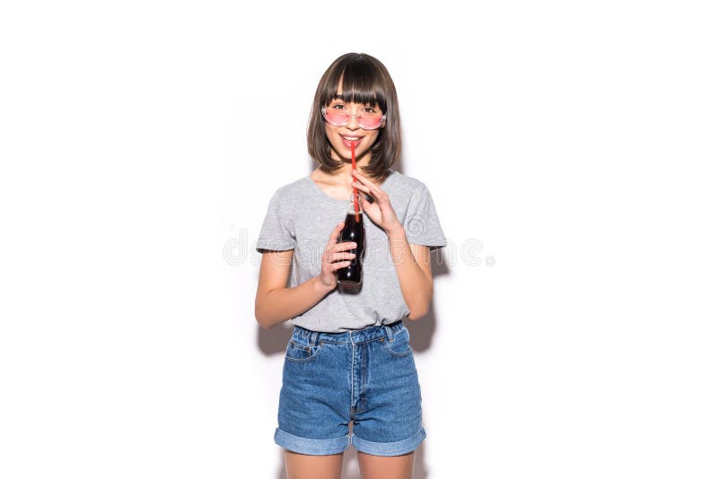 Portrait of beautiful happy cute brunette woman drinking cola from bottle with strsw in casual summer clothes with no makeup