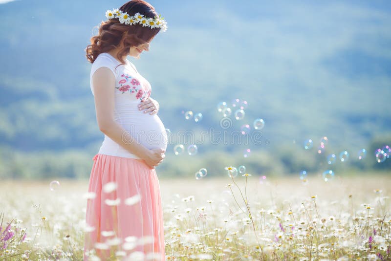 Portrait of beautiful pregnant woman in field blowing bubbles