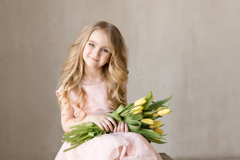 Portrait of very beautiful young pretty girl with yellow flowers tulips, smiling. Indoor photo. Spring theme. Close-up