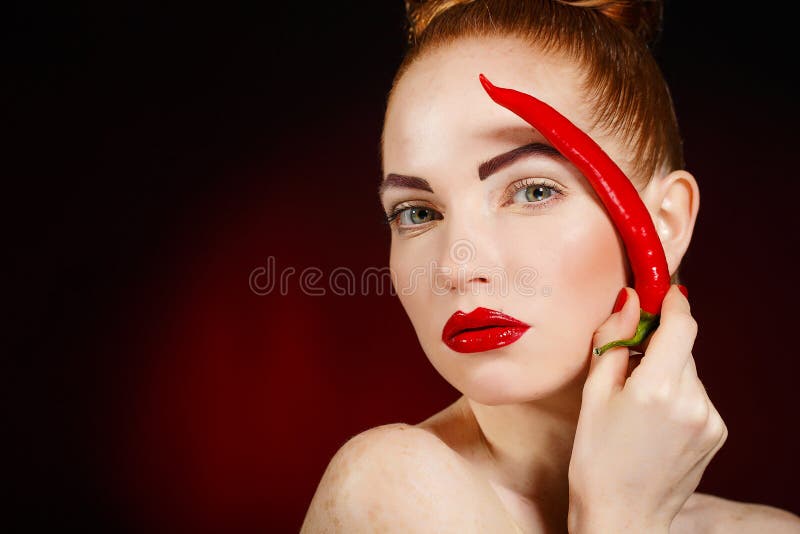 Portrait of beautiful red-haired woman with red hot spicy cayenne chili pepper