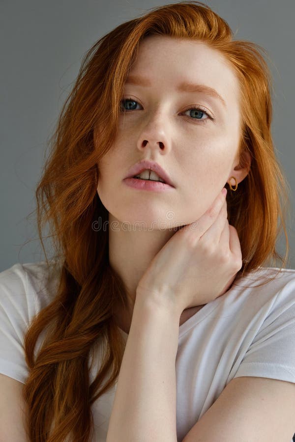 Portrait Of A Beautiful Redhead Girl With Clean Skin Blue Eyes And Freckles In A White T Shirt