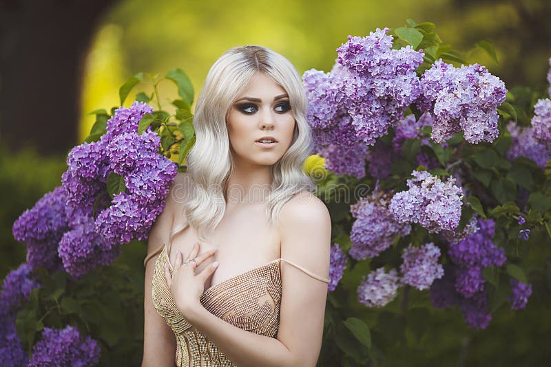 Portrait of a beautiful sensual young blond woman in spring. Blossoming spring garden. Young girl in a gold dress