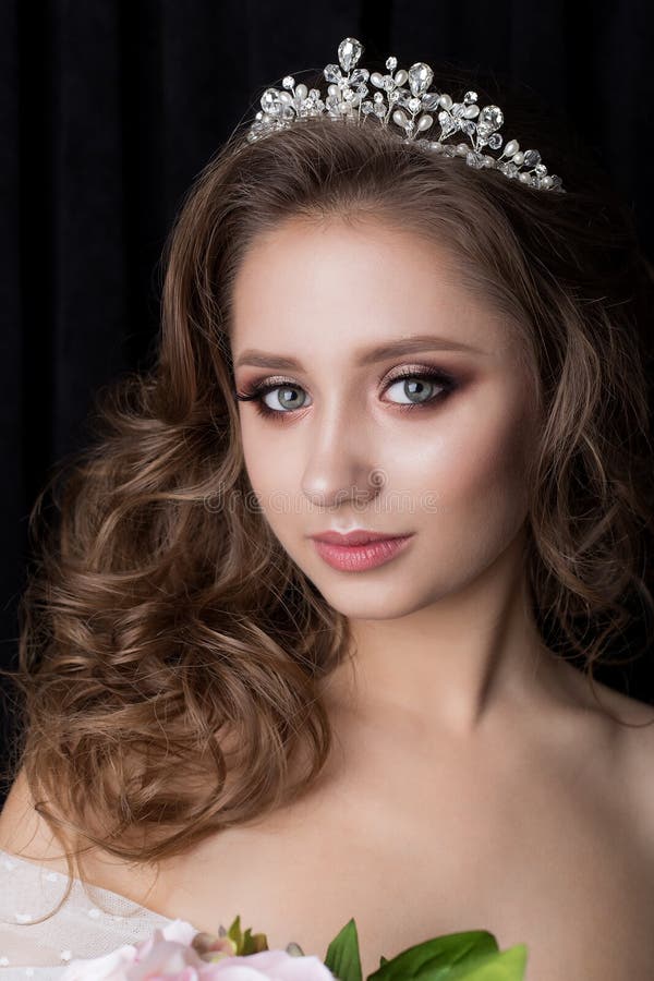 Portrait of a beautiful cute young girl bride with a beautiful wedding ceremony evening hair and makeup with a crown on the h