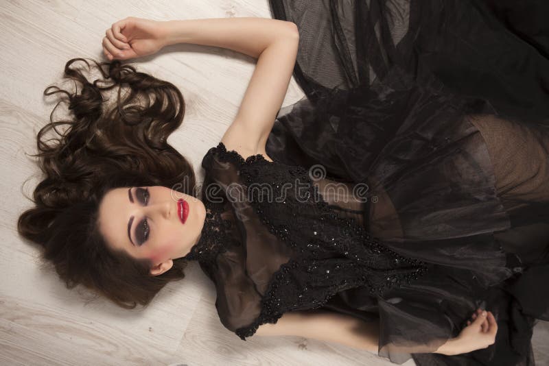 Portrait of beautiful young brunette woman princess in black dress lying down on floor