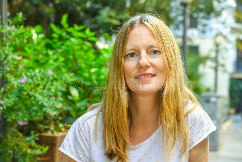 Portrait of beautiful young caucasian woman with long blond hair blue eyes sitting in European American street cafe