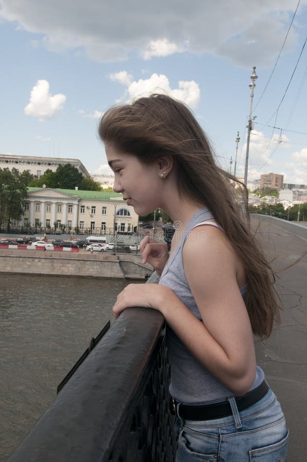 Portrait of beautiful young girl on the bridge blue sky background with blowing hair in wind