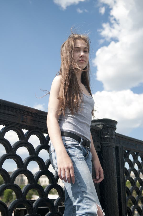 Portrait of beautiful young girl on the bridge blue sky background with blowing hair in wind