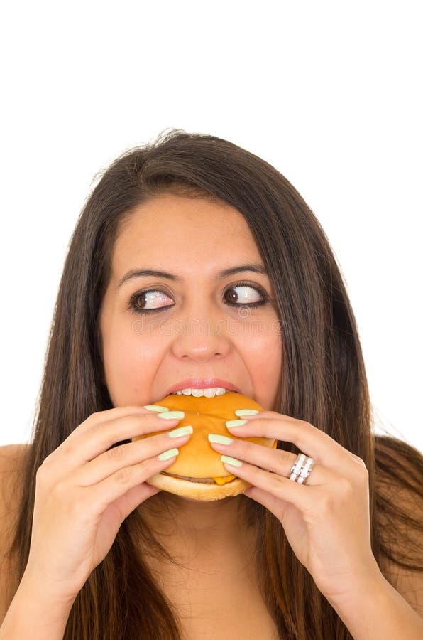 Portrait beautiful young woman posing for camera eating hamburger while making guilty facial expression, white studio stock photography