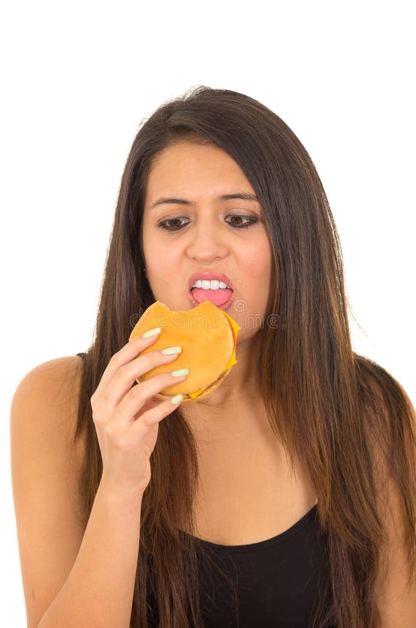 Portrait beautiful young woman posing for camera eating hamburger while making guilty facial expression, white studio royalty free stock images