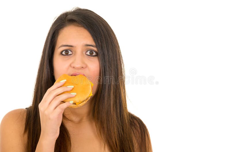 Portrait beautiful young woman posing for camera eating hamburger while making guilty facial expression, white studio stock photography