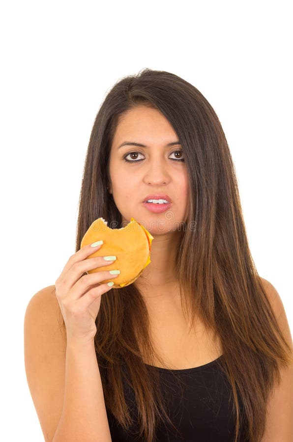 Portrait beautiful young woman posing for camera eating hamburger while making guilty facial expression, white studio royalty free stock photos