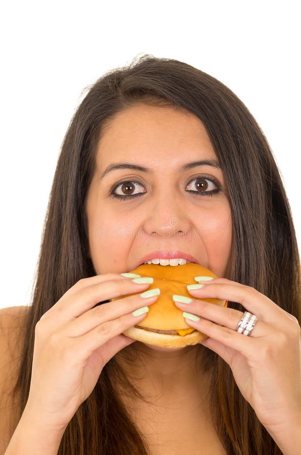 Portrait beautiful young woman posing for camera eating hamburger while making guilty facial expression, white studio royalty free stock images