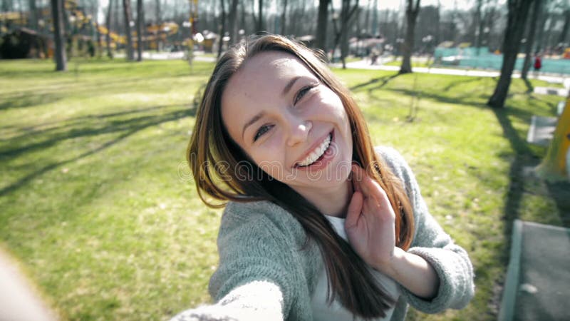 Portrait of a beautiful young woman selfie in the park with a smart phone.