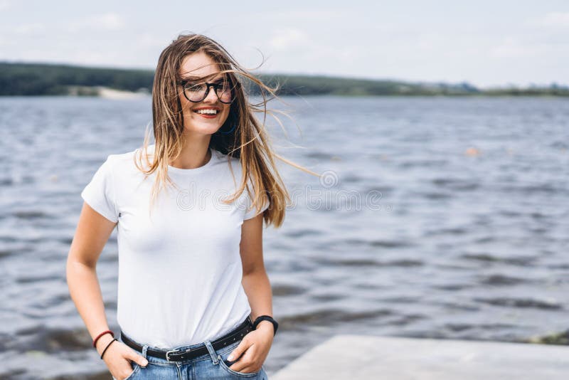 Portrait of a beautiful young woman in stylish glasses. Girl in white tshirt posing on the background of the lake landscape