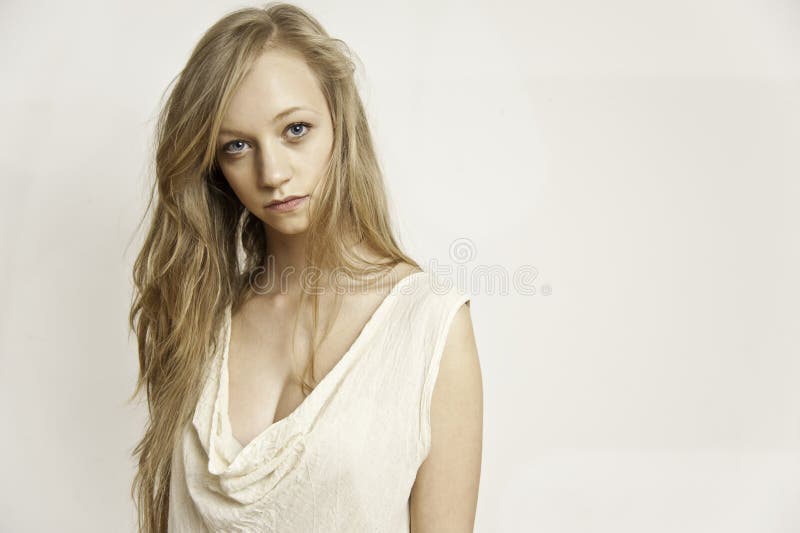 Fashion portrait of a young blonde haired attractive female wearing a light coloured linen dress on an off white background. Fashion portrait of a young blonde haired attractive female wearing a light coloured linen dress on an off white background