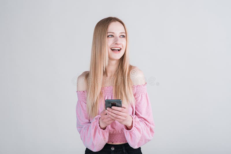 Portrait of a blonde girl holding a smartphone and texting in the studio on a white background.