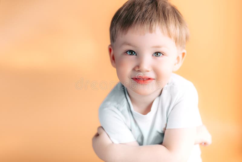 Portrait of blonde happy joyful beautiful cute little boy looking at camera on orange background stock image Portrait of blonde happy joyful beautiful cute little boy looking at camera on orange background stock image
