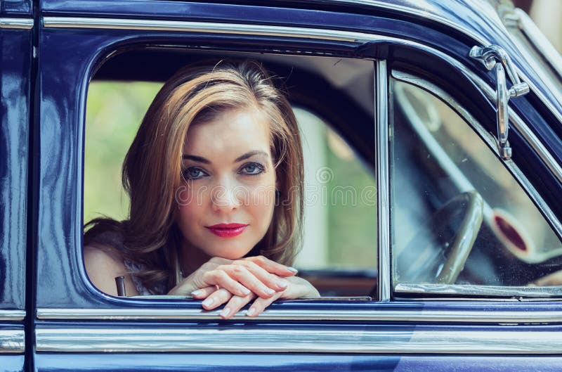 Portrait of blonde woman sitting and looking out of the window of a vintage car artistic conversion