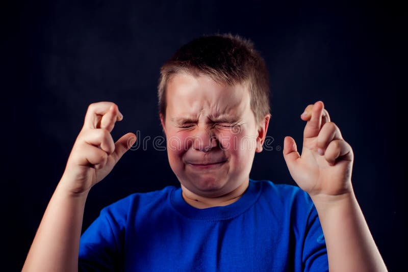 A portrait of a boy with crossed fingers in front of dark background. Children and emotions concept. A portrait of a cute boy with crossed fingers in front of royalty free stock image